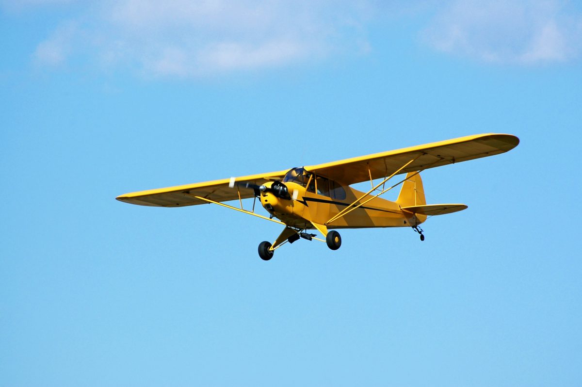 Yellow piper cub airplane flying across blue sky