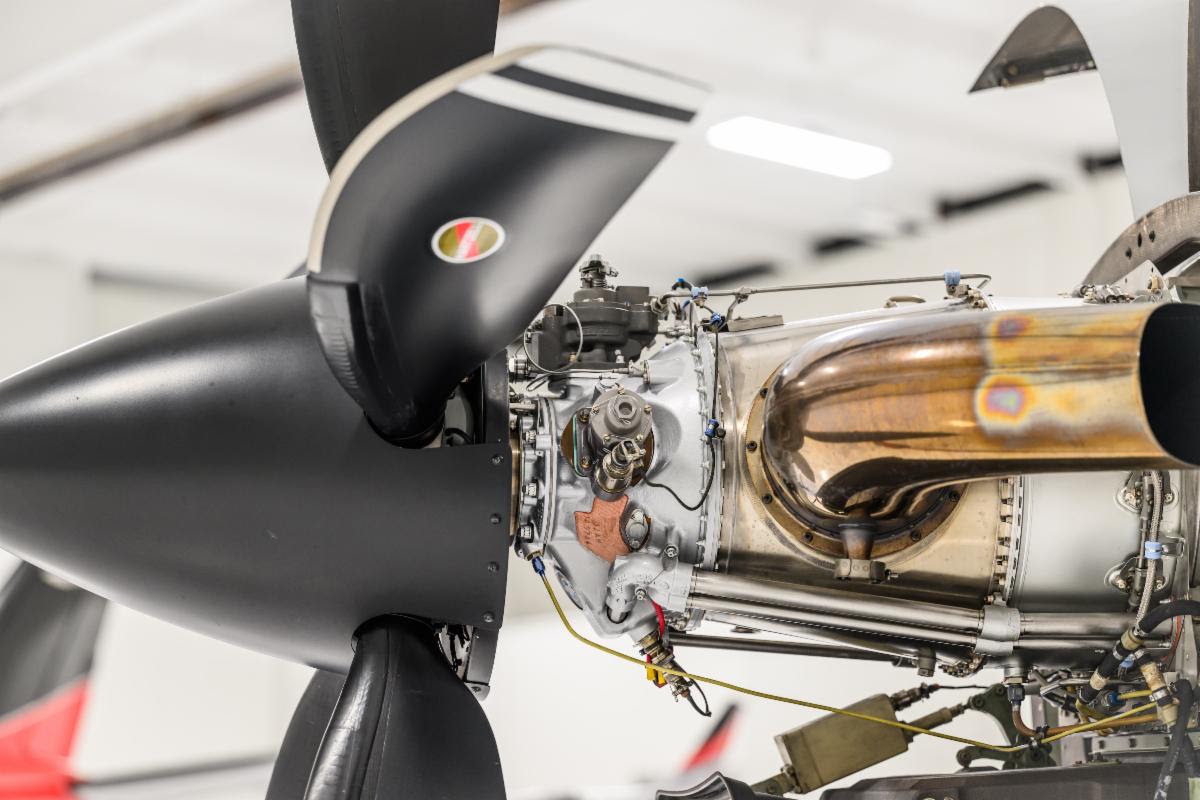 A close-up side shot of a Daher TBM single engine turboprop airplane engine with a five-blade Hartzell Propeller and polished exhaust pipes.